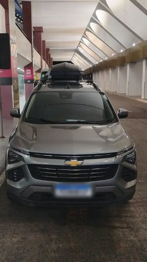 Carro cinza da Sameach, de frente, com o bagageiro no teto, no aeroporto